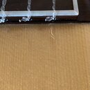 Detailní záběr na spojení hředu a desky akustického nástroje. Vidět jsou tři nylonové struny zakončené uzly. Na dřevěném povrchu desky je viditelná s…