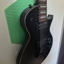 Černá elektrická kytara s matným povrchem a bílým lemováním korpusu. Nástroj má dva humbuckery, tři ovládací knofíky a přepínač. V pozadí je na bílé…
