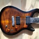 Elektrická kytara s tmavě hnědým přechodem do žluté barvy a výraznou sletovanou strukturou dřeva. Nástroj má dva černý humbuckery, jeden bílý single-…