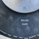Detail spodní strany černé sedací plochy hudebního židle s bílým prošíváním okraje. Na povrchu je vyražen bílý nápis DS750 a pod ním HPN. V horní čás…