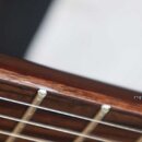 Detailní pohled na hnedý dřevěný hmatník s kovovými pražci a napnutými strunami. Na pravé straně je bílý nápis cigilovic.com. Povrch dřeva vykazuje p…