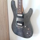 Elektrická kytara s šedým tělem a hrazdivým povrchem. Nástroj má dva humbuckery s bílými plastovými krytkami, jeden tónový knoflík a přepínač. Na těl…