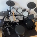 Elektronická bicí souprava značky Roland v černé barvě s bílými bubny. Na bubnech je viditelné logo Roland a nápis V-Drums. Součástí sady je ovládací…