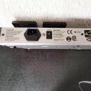 Zadní strana stříbrného elektronického zařízení s několika varovnými nápisy v angličtině a francouzštině. Je zde vidět vstup pro napájení označený sl…