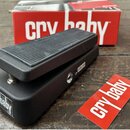 Černý wah-pedál s texturovaným povrchem a gumovou stoupací plochou. Na boku je bílý nápis „cry baby“ a v pozadí je červená krabice s bílým nápisem „c…