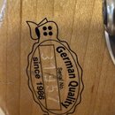 Detail dřevěného povrchu s černým potiskem ve tvaru razítka. Obsahuje nápisy „German Quality“, „Serial No.“ a „since 1986“. Uvedené sériové číslo je…