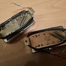 Dvě elektrické kytarové snímače v kovových krytech stříbrné barvy. Na spodní straně obou snímačů je vyražen nápis gibson USA. Snímače mají černé vodi…
