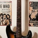 Elektrická kytara s trupem v barevnosti sunburst a černým pickguardem. Na hlavě hmatníku je nápis "Squier STRAT". Nástroj má hmatník z tmavého dřeva…