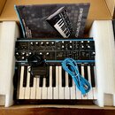 Černý syntetizátor s klaviaturou umístěný v přepravním boxu s bílým polystyrenem. Na horním panelu jsou vidět nápisy HOLTER, OSCILLATORS, MIXER a FIL…