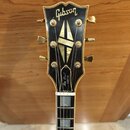 Černá hlava elektrické kytary se zlatým lemováním a zlatými ladičkami. V horní části je bílý nápis Gibson a níže na zvonku nápis Les Paul CUSTOM. Upr…