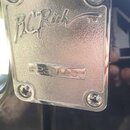 Detail kovového štítku na černé hlavě kytary. Na štítku je vyražen nápis B.C Rich TM a sériové číslo 2230115. Štítek je připevněn čtyřmi šrouby a vyk…