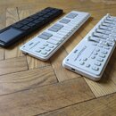Tři bílé a černé MIDI kontroléry z plastu položené na dřevěné podlaze. Uprostřed je klaviatura s nápisem KORG nanoKEY2 a vpravo kontrolér s posuvníky…