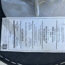 Fotografie detailu spodní strany černého hudebního sedáku s přilepenou bílou informativní nálepkou. Na nálepce jsou texty v angličtině, francouzštině…