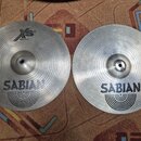 Dvě stříbrné kovové činely značky SABIAN s koncentrickým žilováním povrchu. Levý činele má v horní části logo XS, nápis 20 a text Hata W736 cm. Oba n…