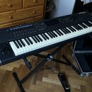 Černý digitální klavír s bílými a černými klávesami, umístěný na černém X-stojanu. V pravém horním rohu je bílý nápis KURZWEIL PC3. Na ovládacím pane…
