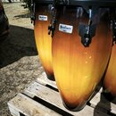 Tři kongy s gradientem od černé barvy u horního okraje po žlutou v prostřední části. Na každém nástroji je viditelný bílý obdélníkový štítek s nápise…