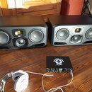 Dva černé studiové monitory s třemi reproduktory každý a žlutými detaily v horní části. Před nimi leží černý audio rozhraní s bílým logem a nápisem B…