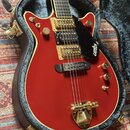 Červená elektrická kytara s gold hardwarem v černém tvrdém kufru. Na černé plechovce je bílý nápis GRETSCH. Nástroj má dva snímače, zlaté knoflíky a…