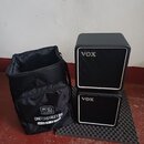 Na fotografii je černý textilní přepravní vak a dva černé kostkovité reproduktory s bílým lemováním. Na vaku je bílý nápis „acus sound engineering“ a…