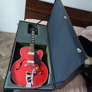 Červená polodubová elektrická kytara v černém tvrdém kufru. Na hlavě hmatníku je viditelné logo Gretsch a na kovovém krytu mostu nápis Guild. Nástroj…