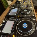 Sada DJského vybavení značky Pioneer DJ umístěná na dřevěném stole. V popředí je vidět přehrávač s nápisem Pioneer DJ a označením modelu CDJ-3000, kt…