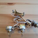 Fotografie zobrazuje elektronický zapojovací set pro kytaru, který obsahuje dva potenciometry a jeden přepínač s kovovými hřídelmi. Komponenty jsou p…