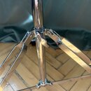Detail spodní části chromovaného stativu s rozkládacími nohami. Povrch je lesklý, v místech spojů a na spodní části středové tyče jsou vidět drobné š…
