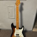 Elektrická kytara s trupem v barevnosti sunburst a bílým pickguardem. Na hlavě hmatníku je viditelné logo Squier. Krk a hmatník jsou vyrobeny ze svět…