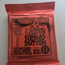 Červené balení kytarových strun s černými nápisy a obrázkem orla. Na obalu je uveden název značky ERNIE BALL, model 7-STRING SKINNY TOP HEAVY BOTTOM…