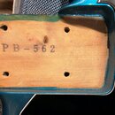 Detail dřevěné části zadní strany modrého nástroje. Na světlém dřevě je černý nápis PB-562 a čtyři otvory pro šrouby. Povrch dřeva vykazuje drobné ne…