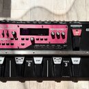 Černý loop pedal s růžovým předním panelem. Na přístroji jsou nápisy BOSS RC-50 LOOP STATION, ALL START/STOP a označení stop v podobě tří šipek směřu…