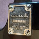 Detail kovového šiltíku na zadní straně hnedu hnědé kytary. Na šiltíku je logo samick a nápis MADE IN KOREA SINCE 1958. Uprostřed je nalepený štítek…