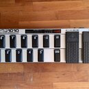 Stříbrný MIDI kontrolér s černými spínači a dvěma expresními pedály. Na horní straně je nápis FCB1010 MIDI FOOT CONTROLLER a na jednom z pedálů logo…