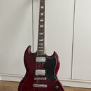 Kytara s tmavě červeným lakem a černým pickguardem. Na hlavě je viditelné zlaté logo Epiphone. Nástroj má dva humbuckery, tři ovládací knoflíky a pře…