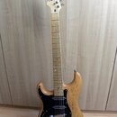 Elektrická kytara s přírodním dřevěným povrchem těla a hnedým hracím hřidlem. Na hlavě je viditelné logo BACHA. Kytara má černý pickguard, tři snímač…