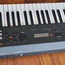Černý klavírní syntetizátor s bílými a černými klávesami. Na levém boku je svisle napsáno mx49 a v levém dolním rohu je logo YAMAHA. V pravém dolním…