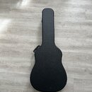 Černý tvrdý kufr na kytaru v akustickém tvaru. Povrch je matný a bez viditelných značek či log. Kufr leží na světlé laminátové podlaze.