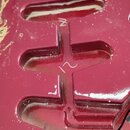 Detail červeného lakovaného těla elektrického nástroje s třemi vyfrézovanými dutinami pro snímače. Na povrchu jsou vidět drobné nečistoty, prach a v…