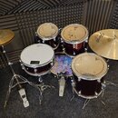 Sada červených bubnů s kovovým hardwarem a mosaznými činely. Na blbáku je vidět logo Sabian, na ostatních bubnech jsou nečitelné loga. Soubor obsahuj…