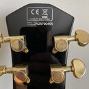 Zadní strana černé hlavy kytary se zlatými ladicími mechanismy. V horní části je bílý obdélníkový rám s logem CE, symbolem přeškrtnuté popelnice a ná…