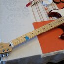 Elektrická kytara s hnědým sunburst povrchem těla a světle hnědým javorovým hmatníkem. Na hlavě je viditelné logo Fender a nápis STRATOCASTER. Tělo m…