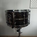 Černý snare drum s chromovaným obručováním a hardwarem, umístěný na chromovaném stojanu. Na koruse nejsou viditelná žádná loga ani nápisy. Povrch nás…