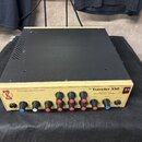 Krémový hybridní basový zesilovač s černým kovovým krytem. Na předním panelu je nápis „The Traveler 550“, „Twin Triode Tube Pre Amplifier“ a „Hybrid…