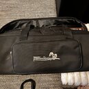 Černá látková přepravní taška s rukojtí a přední kapsou. Na přední kapse je bílý nápis Palmer pedalbay EPS doprovázený siluetou koní. Taška je v dobr…