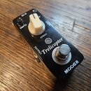 Černý efekt pedál s kovovým šasi. Na horní straně jsou nápisy MOOER, Trelicopter, SPEED, DEPTH, INPUT, OUTPUT a DC IN. Pedál má jeden bílý ovládací k…