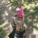 Černá elektrická kytara s výrazným, ostře hranatým tvarem těla a hlavy. Na hlavě je bílý nápis B C Rich. Kytara má dva humbuckery, hnedový hmatník a…