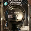 Černá sluchátka v originálním plastovém obalu. Na horní části obalu je nápis ROCKMAN ACE a texty propagující funkce zařízení. Uprostřed je seznam ACE…