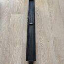 Černý, úzký a vysoký lineární reproduktor s mřížkovým povrchem. Uprostřed je umístěno bílé logo BOSE. Nástroj leží na dřevěné podlaze a vykazuje čist…