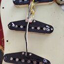 Tři elektrické snímače typu single-coil s černými plastovými kryty a bílým spodním základem. Snímače jsou umístěny na krémovém pickguardu a jsou prop…