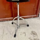 Černý bubenířský židle s kovovým chromovaným stojanem a třínožkou. Na sedáku je bílý nápis TAMA a pod ním text THE STRONGEST NAME IN DRUMS. Povrch se…